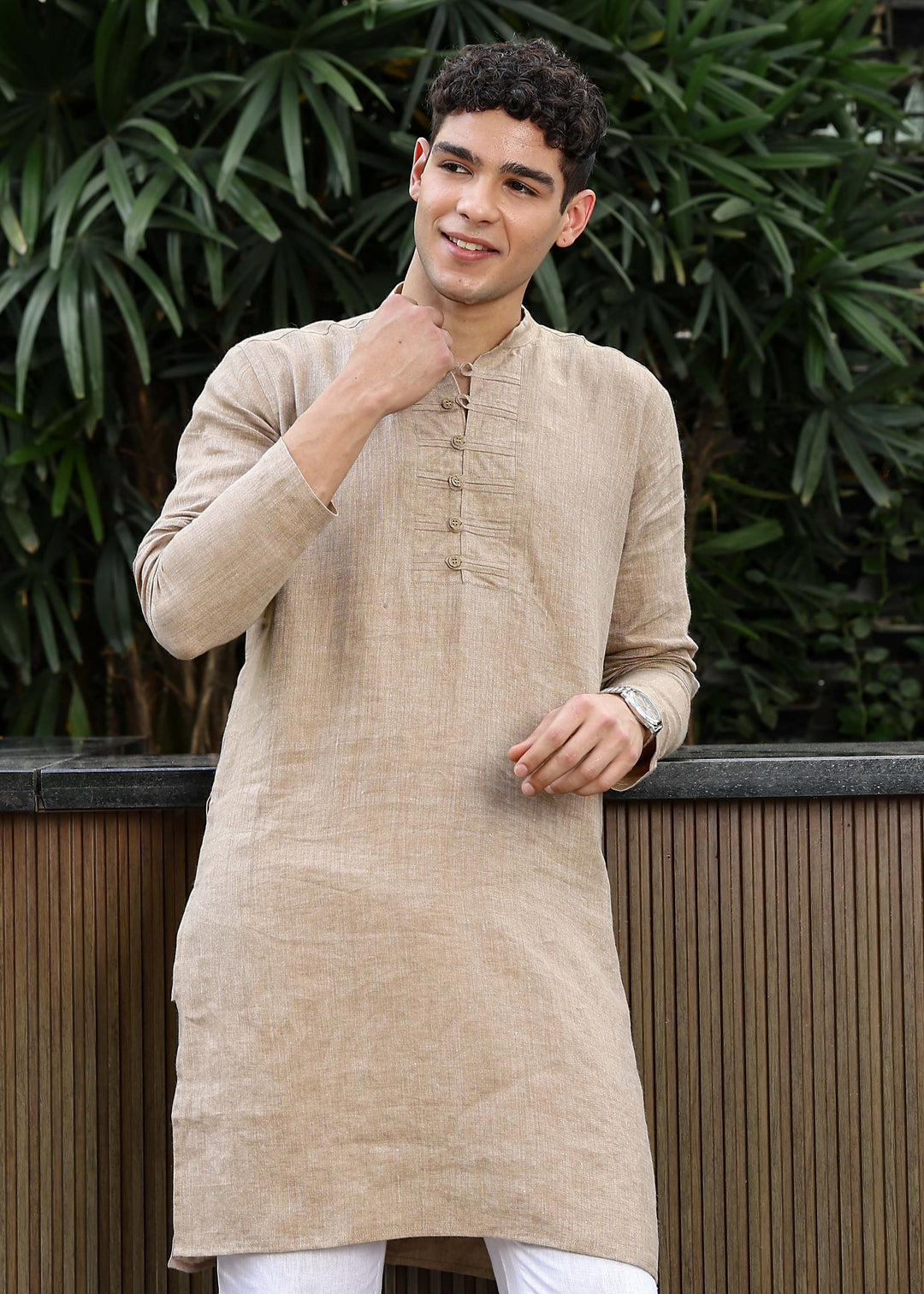 Man wearing a 100% mocha 60 lea Kurta, with placket detail, in a Green outdoor Background.