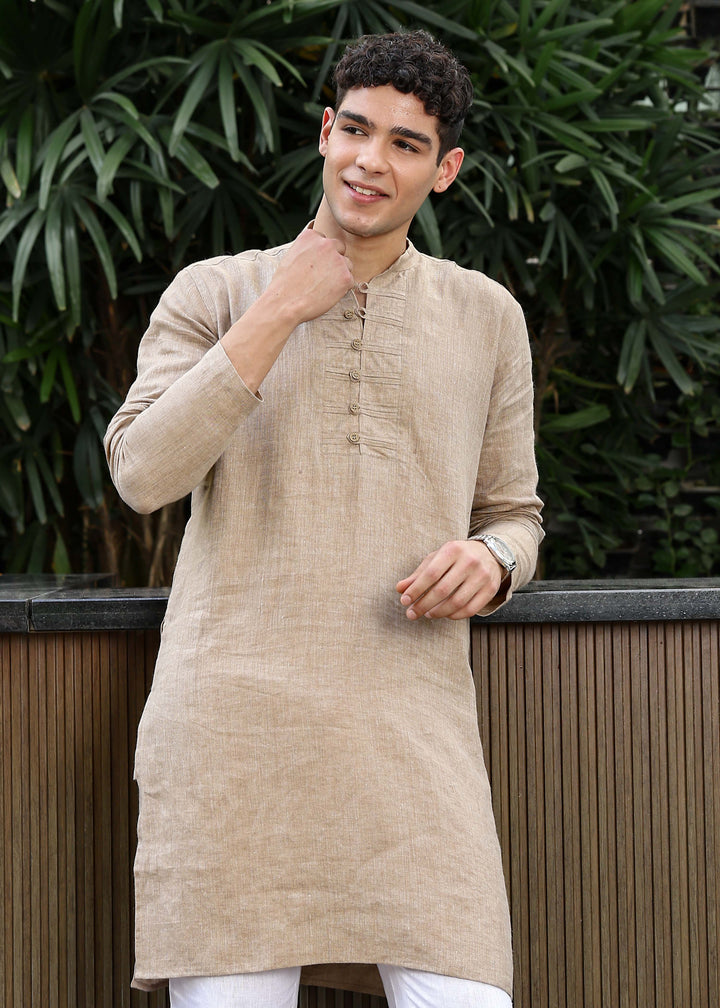Man wearing a 100% mocha 60 lea Kurta, with placket detail, in a Green outdoor Background.
