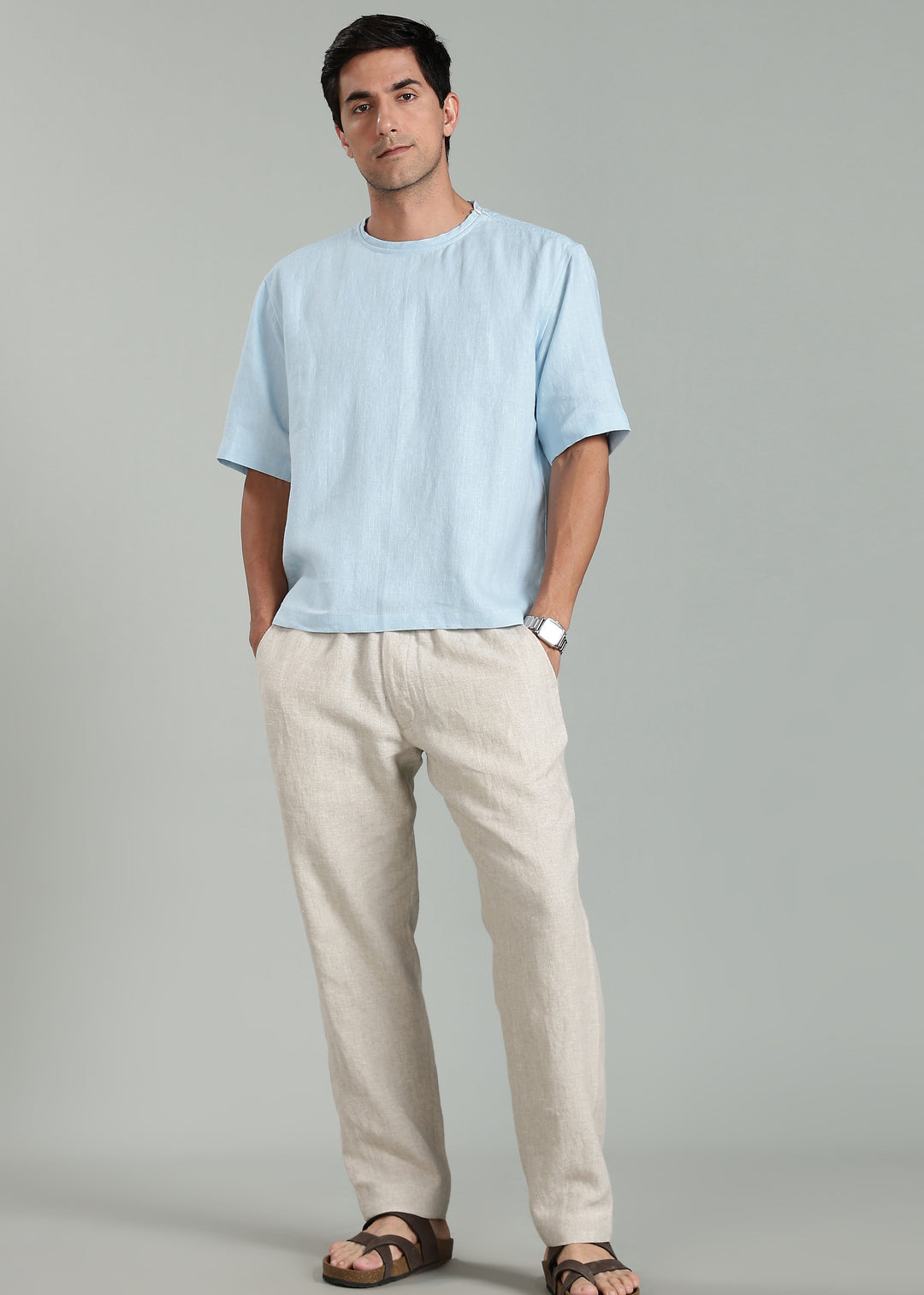 Man wearing a light blue pure linen tshirt and beige pure linen pants against a gray background