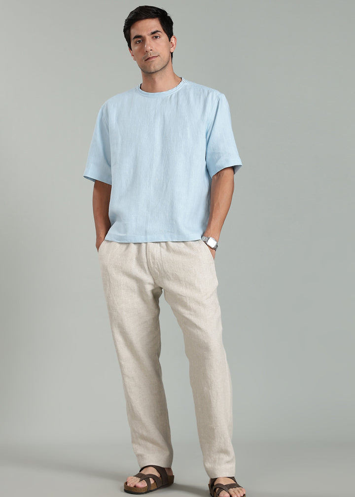 Man wearing a light blue pure linen tshirt and beige pure linen pants against a gray background