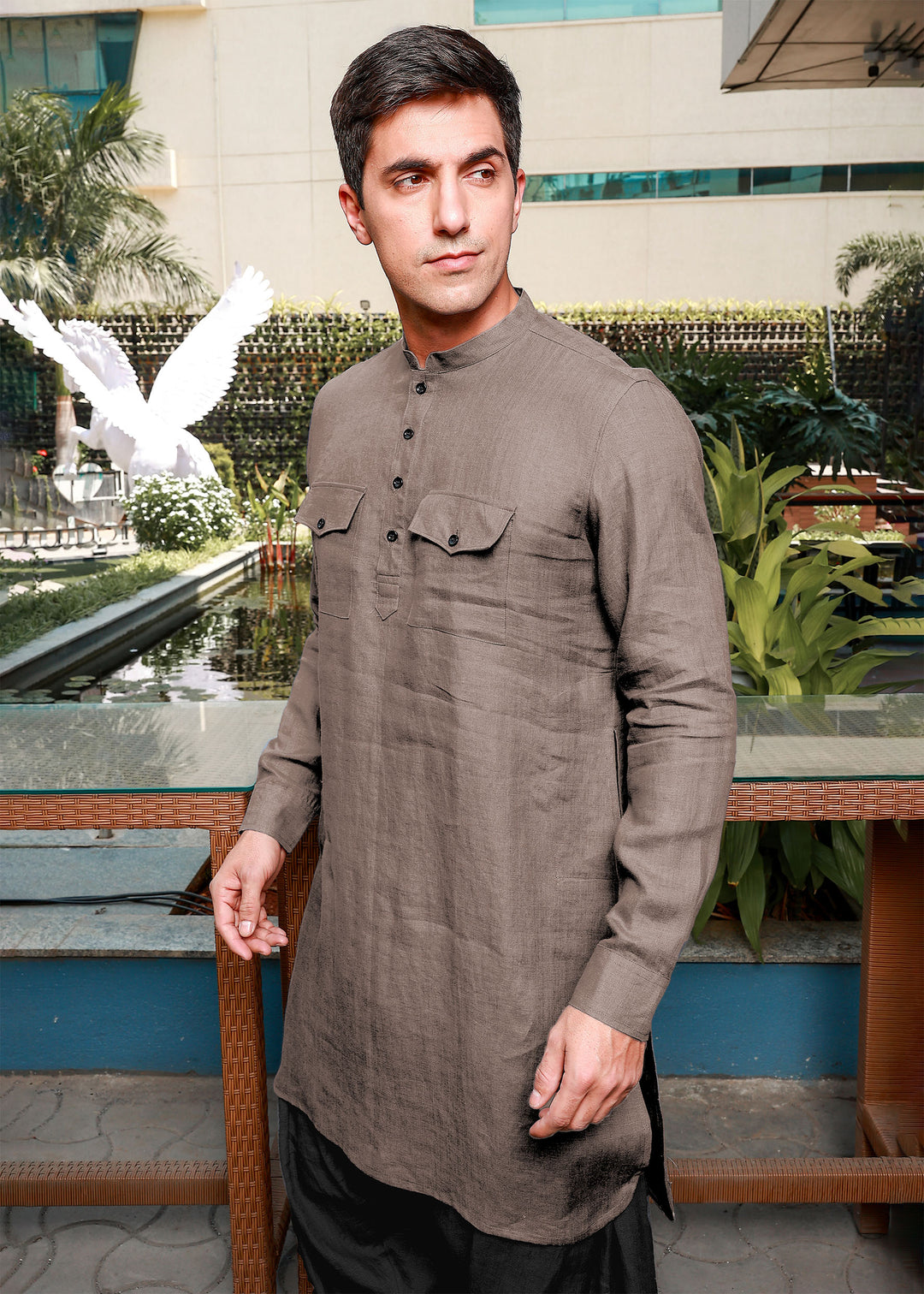 Man wearing a 100% pure linen fawn pink long kurta standing in front of a decorative garden.