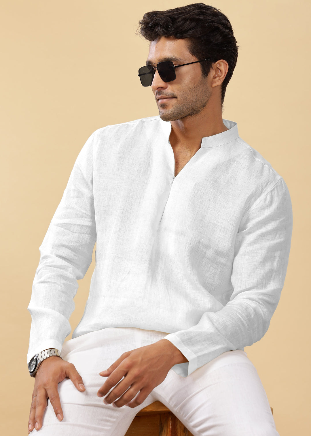 A man wearing a white full-sleeve broad-notched collar pure linen short kurta, sitting with a casual pose.