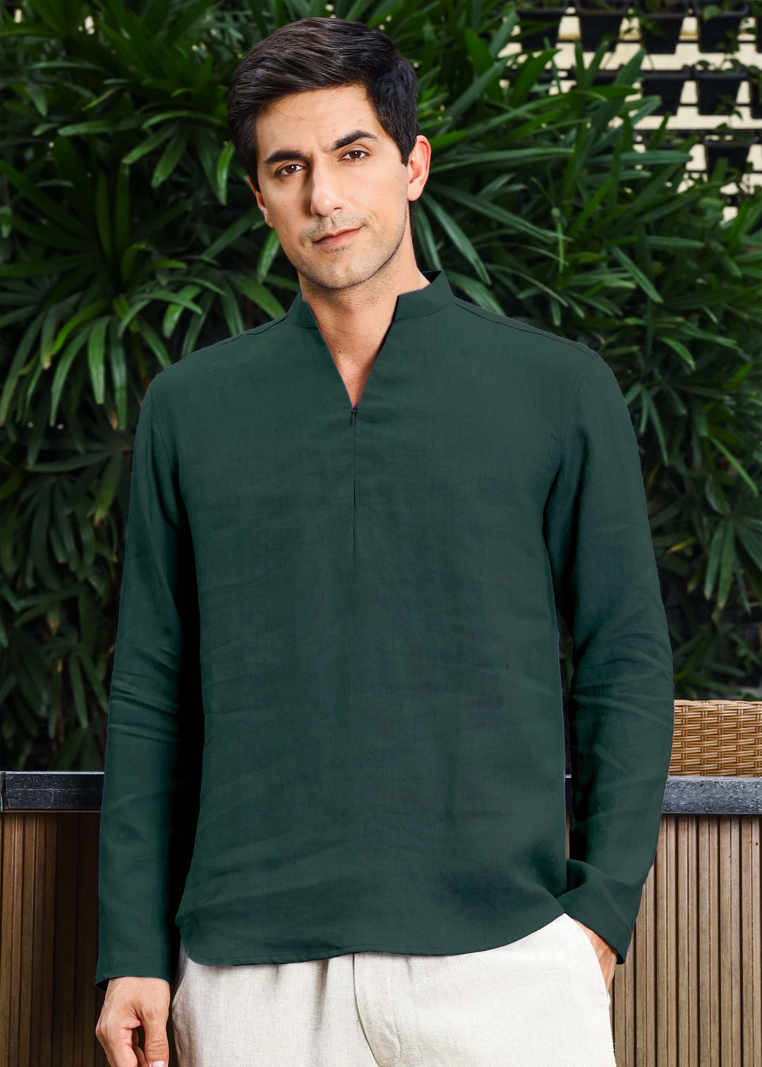 Man wearing a green long-sleeve shirt standing outdoors with greenery in the background