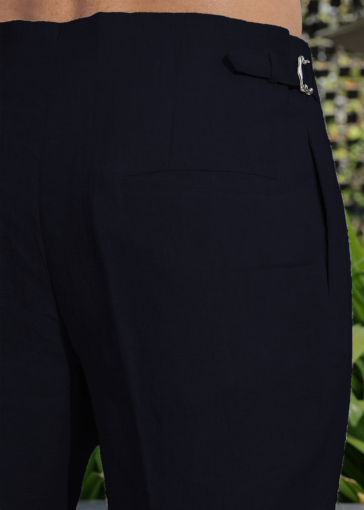 Close-up of 100% pure linen regal blue pants with a button detail, blurred green background