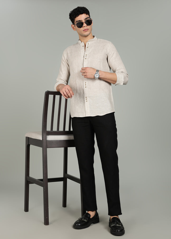 Man wearing a a 100% pure linen ecru full sleeve shirt in 60 LEA and black pants standing next to a chair on a gray background