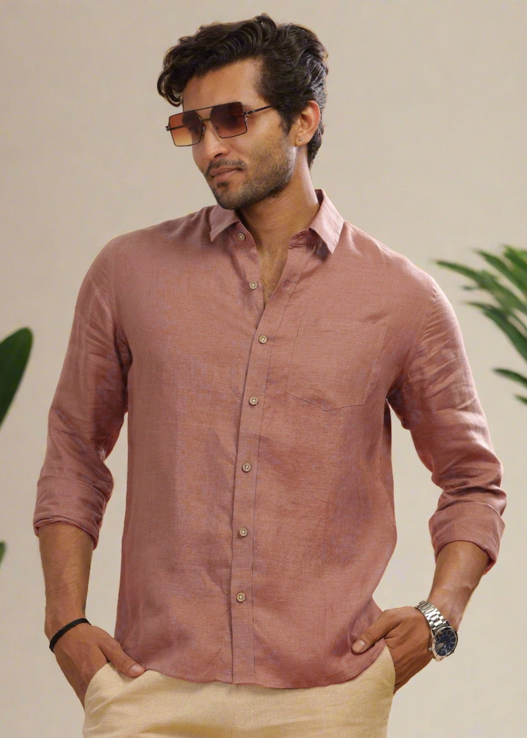 Man wearing a 100% pure linen fondue pink full sleeve shirt with sunglasses and a watch, standing against a neutral background with greenery.