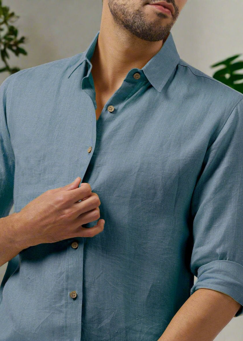 A close-up of a man wearing a blue grey, pure linen, full sleeve shirt with a regular collar and button-up front.