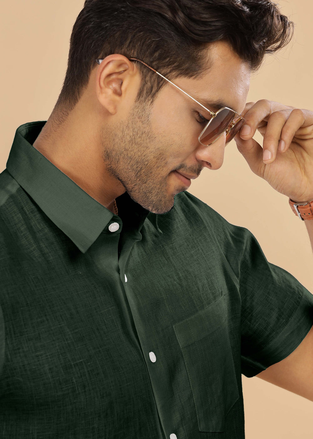 Man adjusting sunglasses while wearing a 100% pure linen dark fern green shirt in a beige background