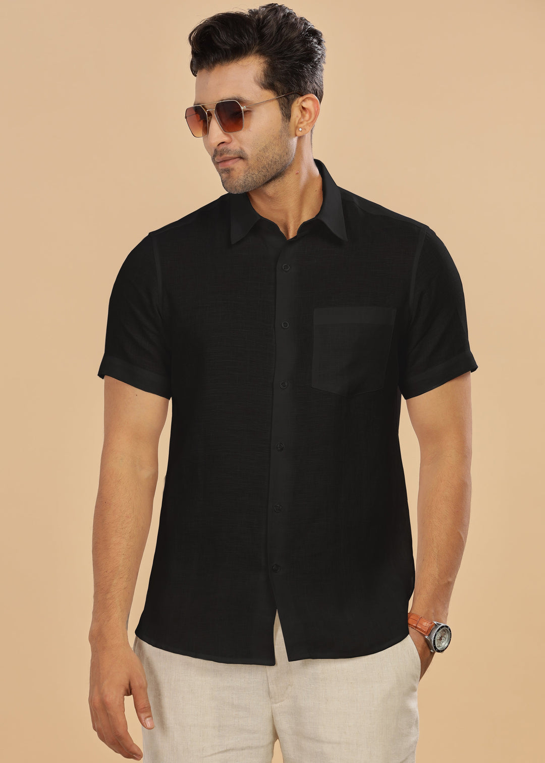 Man wearing a black short-sleeve shirt and sunglasses on a beige background