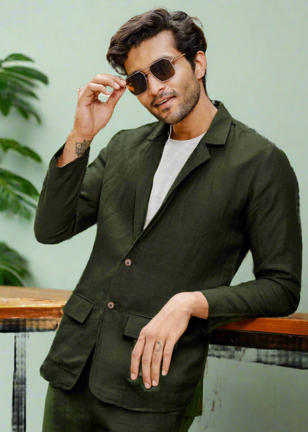 A man wearing a dark green deconstructed pure linen jacket with double pockets, paired with a white shirt and dark green trousers.