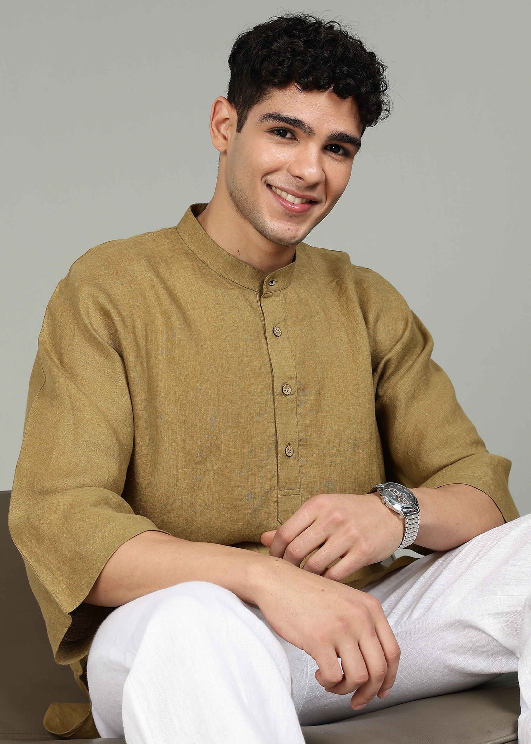 Man wearing a 100% pure linen golden olive green short kurta in 60 LEA with white pants against a gray background