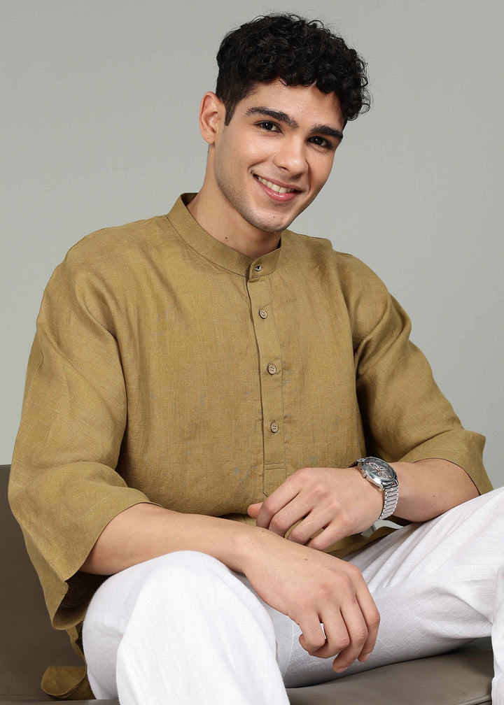Man wearing a 100% pure linen golden olive green short kurta in 60 LEA with white pants against a gray background