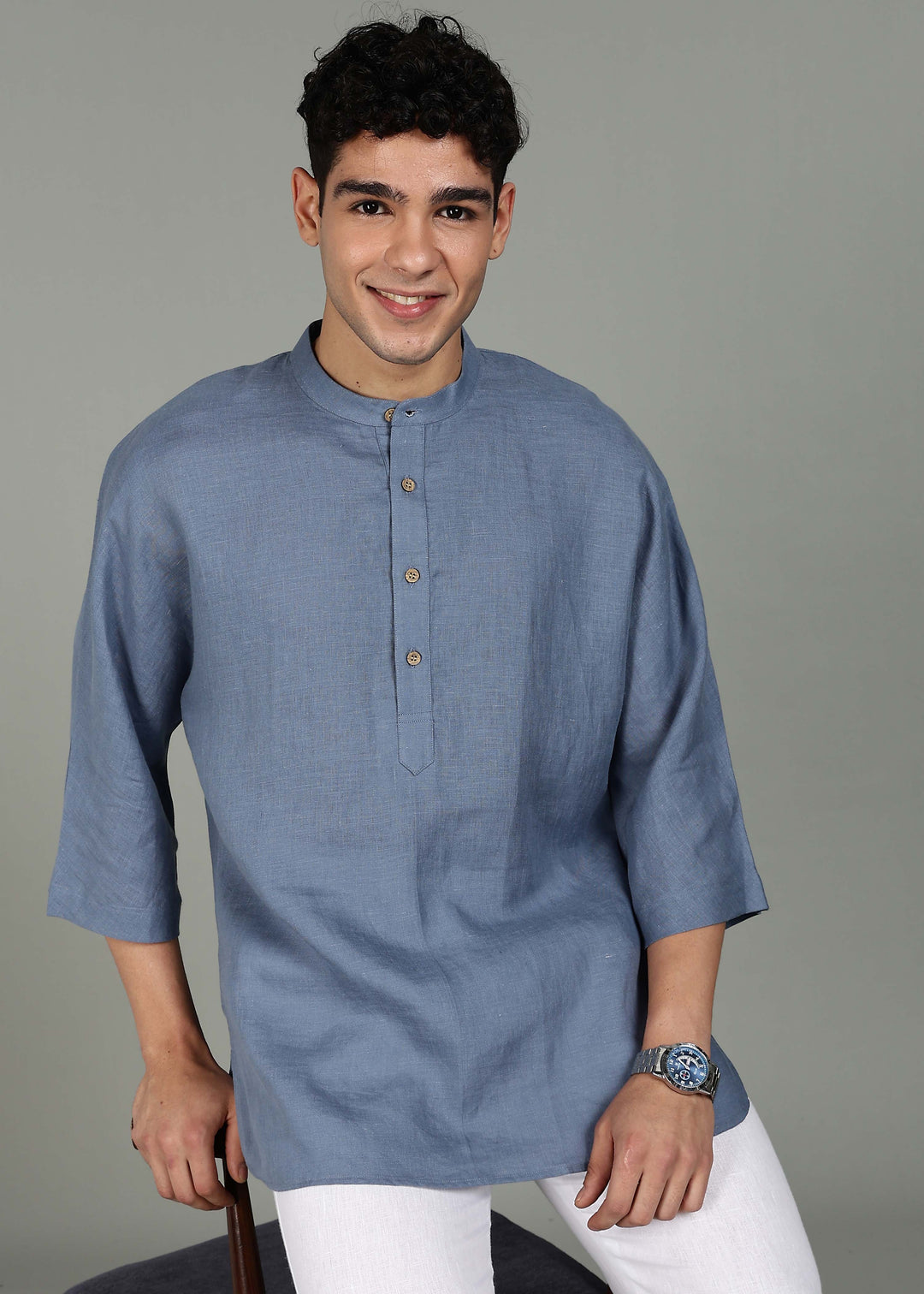 Man wearing a 100% pure linen blue grey short kurta in 60 LEA with white pants against a gray background