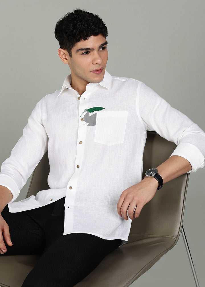 Man wearing a 100% pure linen white shirt in 44 LEA with elephant embroidery sitting on a chair against a gray background