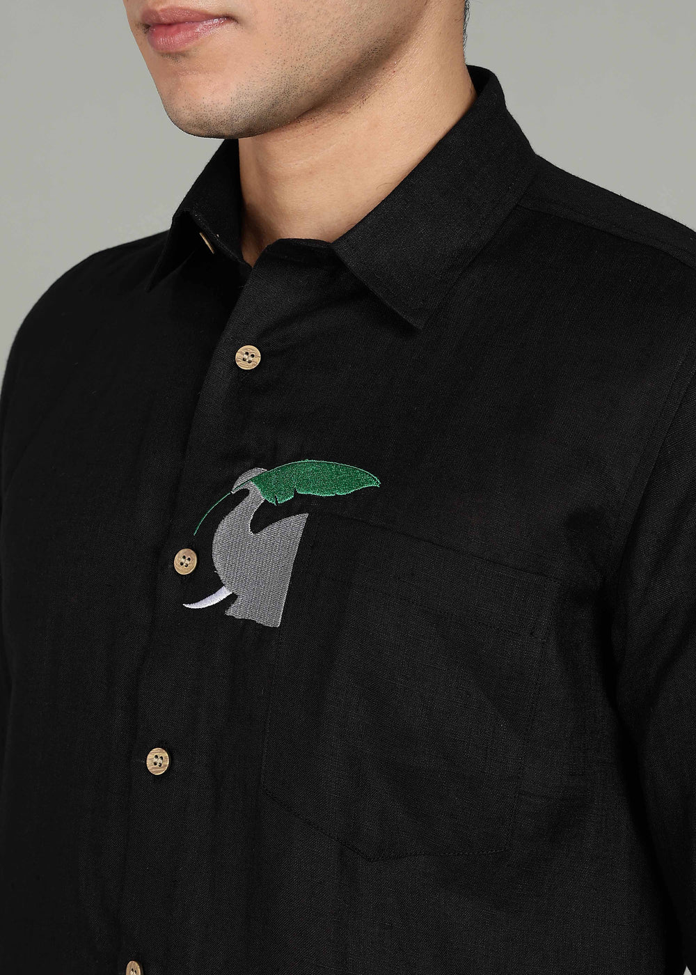 Man wearing a 100% pure linen black shirt in 60 LEA with elephant embroidery against a gray background