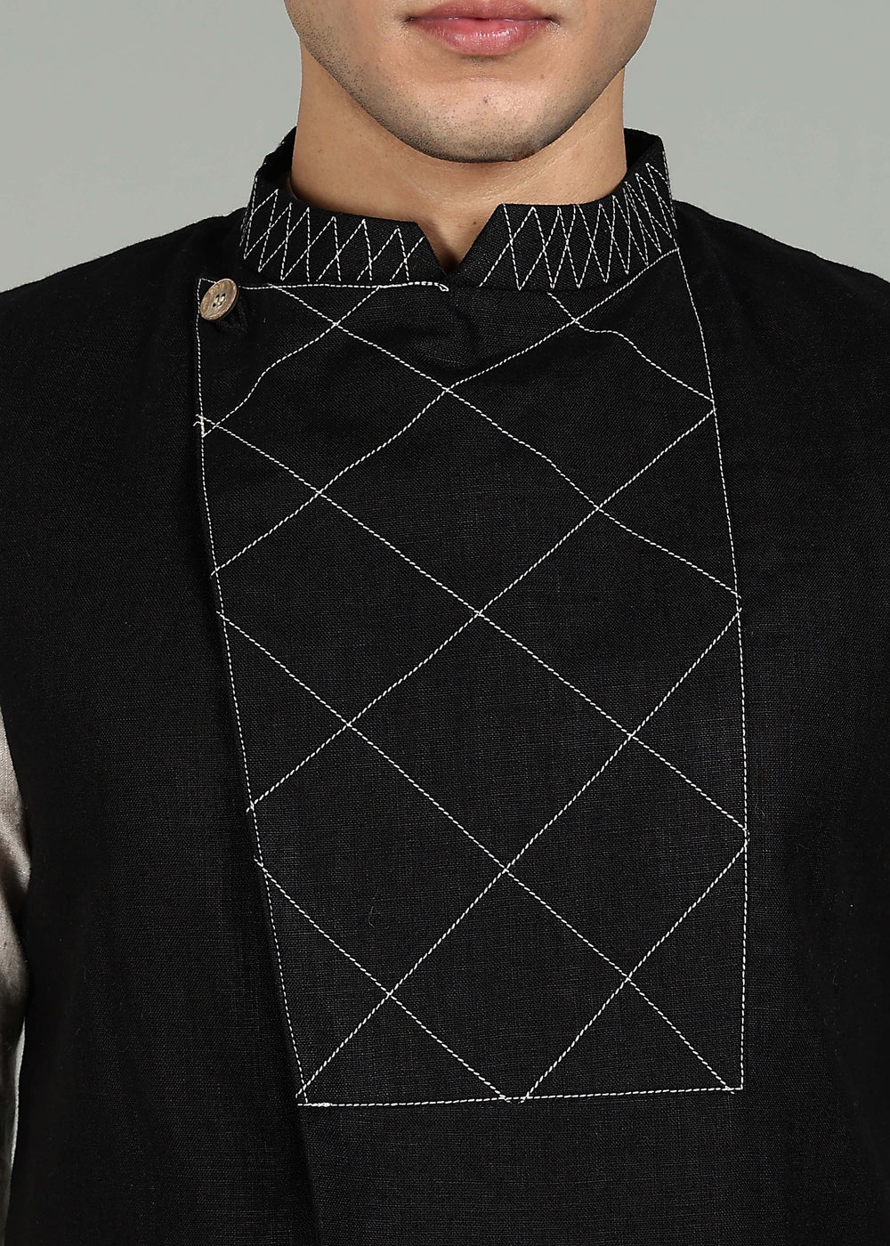 Man wearing a black embroidered 100% pure linen vest in 25 LEA over an ecru shirt on a gray background