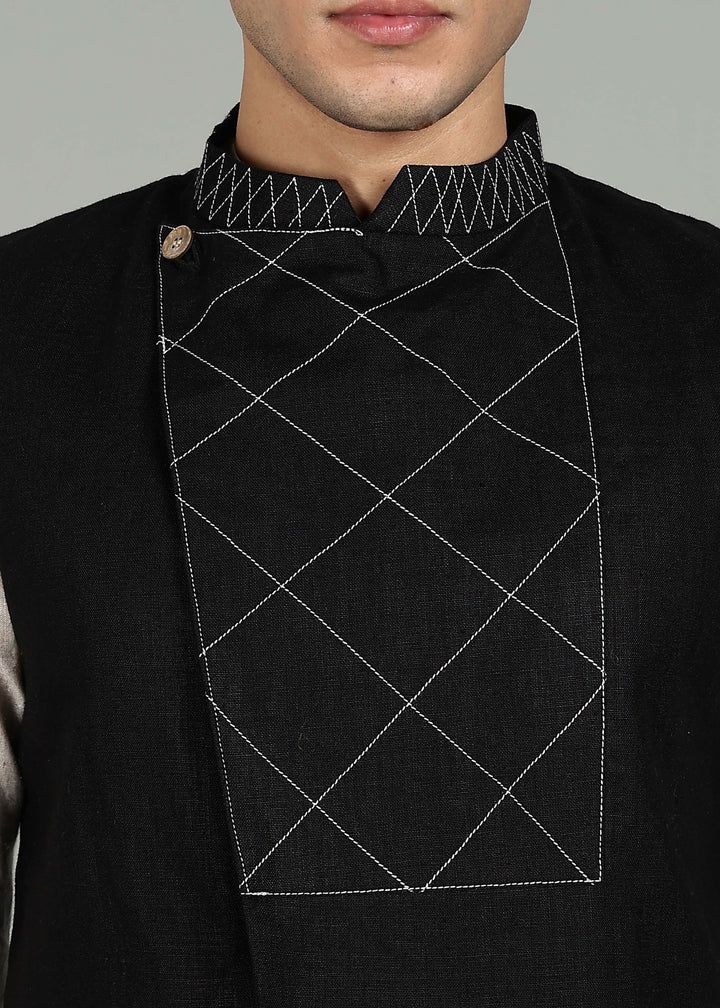 Man wearing a black embroidered 100% pure linen vest in 25 LEA over an ecru shirt on a gray background