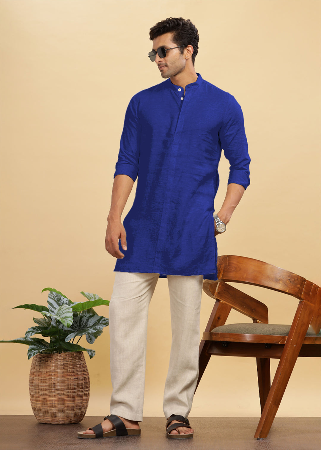 Man wearing a 100% pure linen egyptian blue kurta with beige pants standing in a room with a plant and chair.