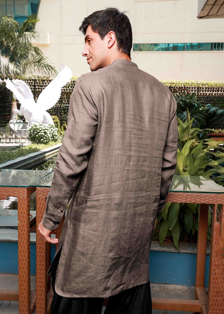 Man wearing a 100% pure linen fawn pink long kurta standing on a balcony with plants and a building in the background