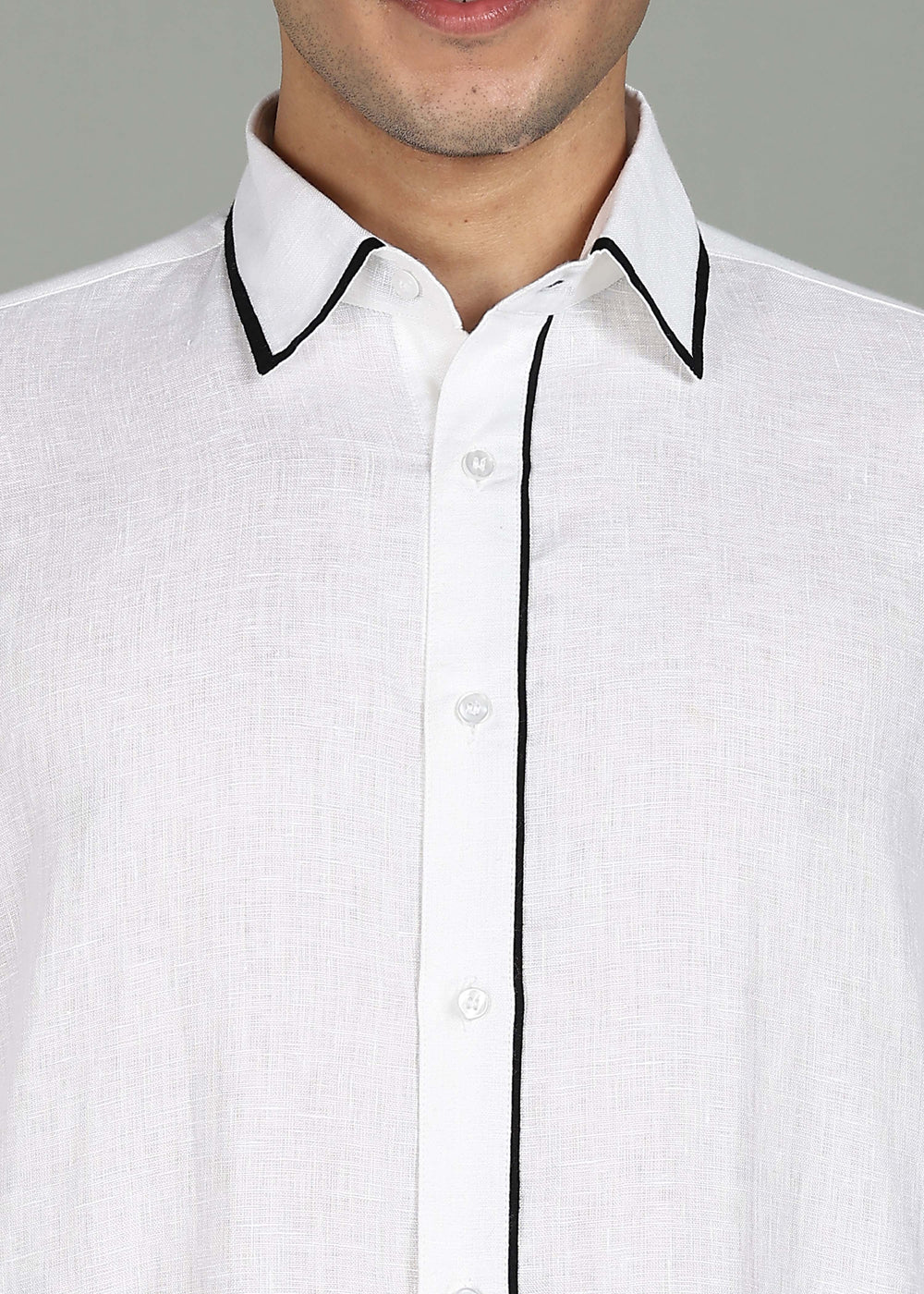 Man wearing a 100% pure linen white long kurta in 44 LEA with black piping detail with a gray background