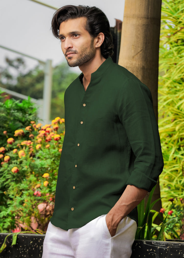 Man wearing a 100% pure linen dark fern green shirt standing outdoors with greenery in the background