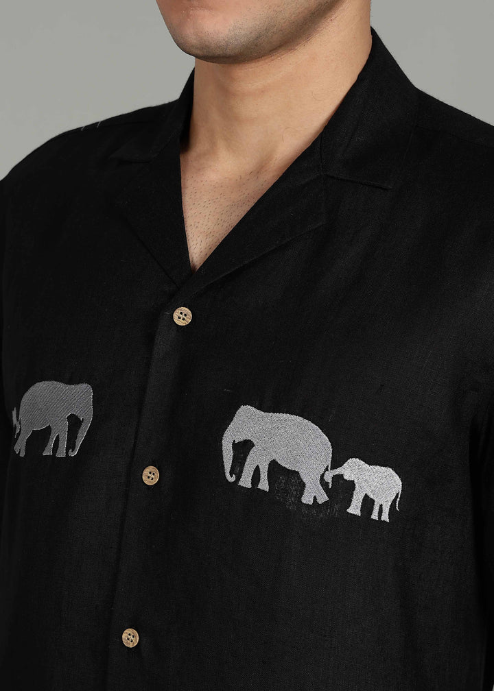 Man wearing a 100% pure linen black shirt in 60 LEA with elephant embroidery on a gray background