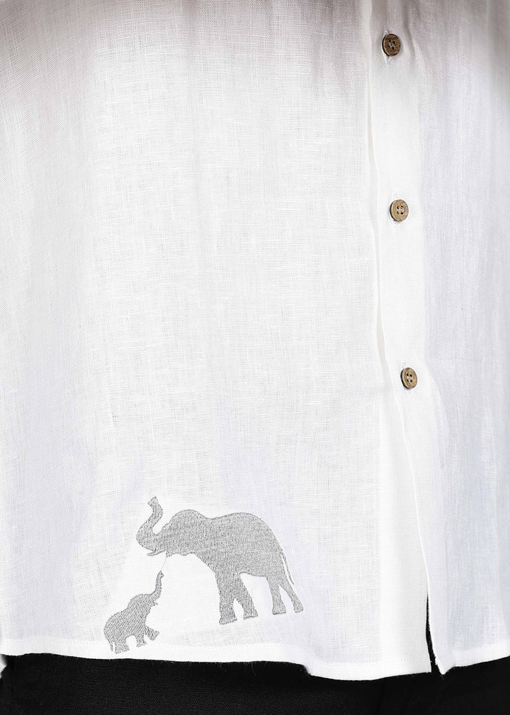 Man wearing a 100% pure linen white shirt in 44 LEA with elephant embroidery sitting on a chair against a gray background