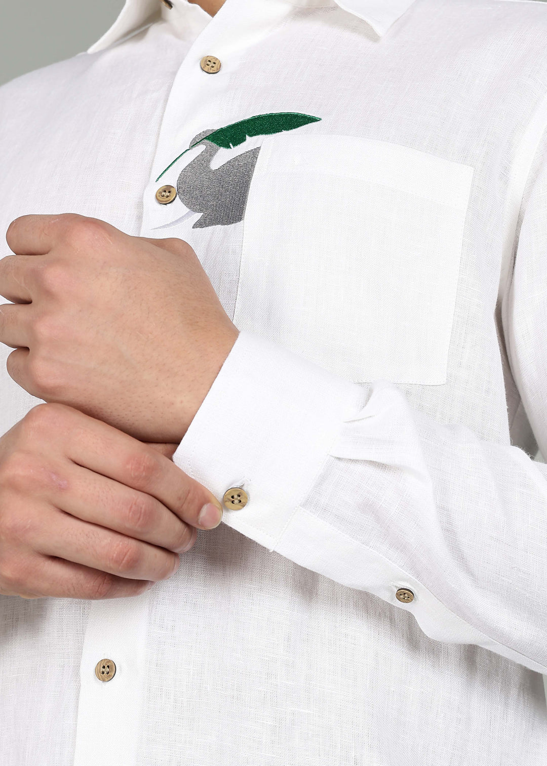 Man wearing a 100% pure linen white shirt in 44 LEA with elephant embroidery sitting on a chair against a gray background