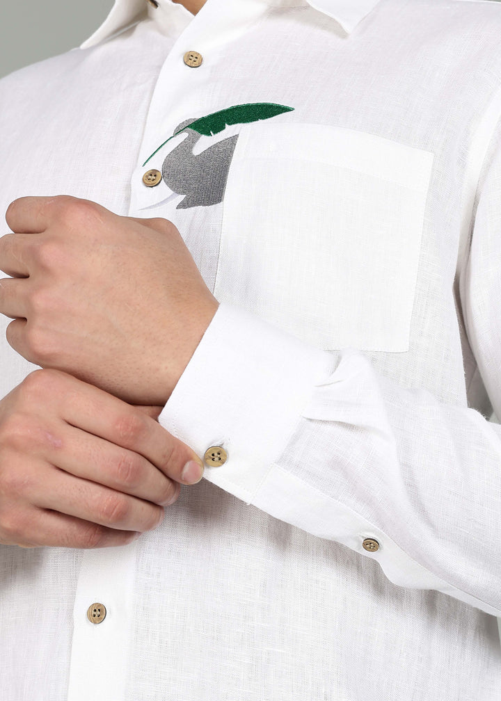 Man wearing a 100% pure linen white shirt in 44 LEA with elephant embroidery sitting on a chair against a gray background