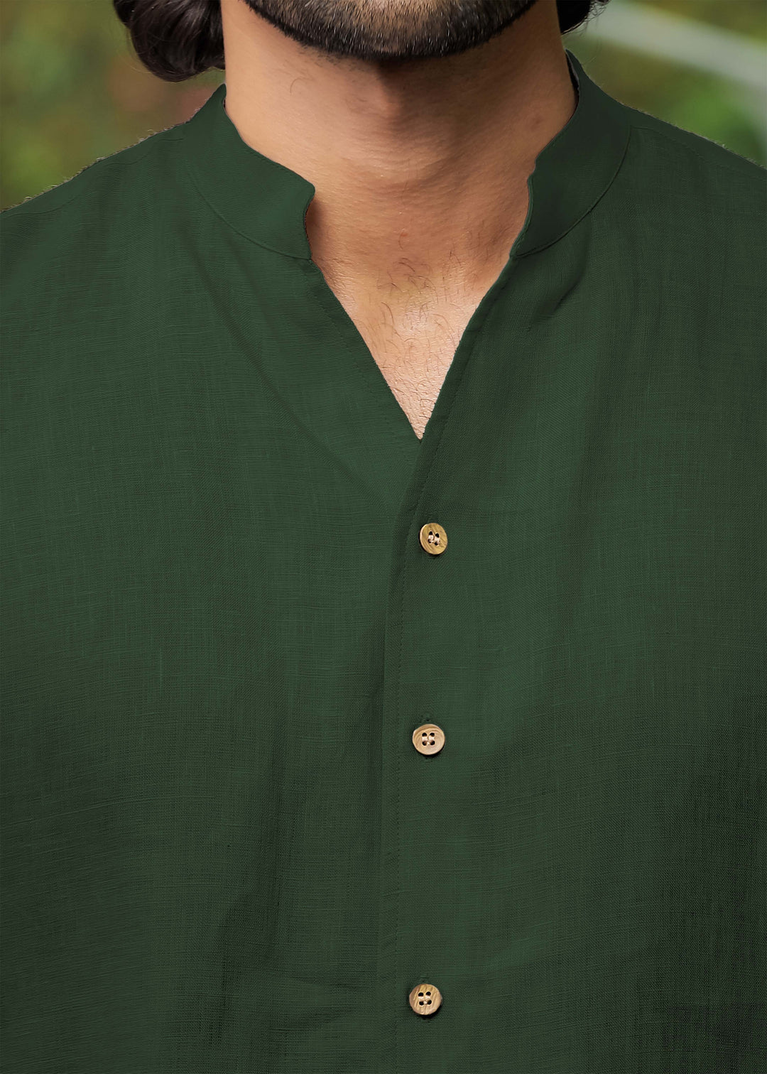 Close-up of a person wearing a 100% pure linen dark fern green shirt against a blurred background