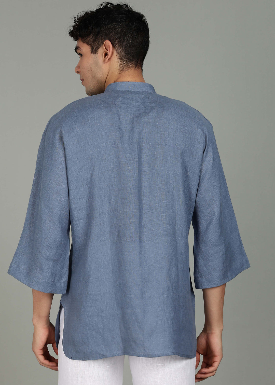 Man wearing a 100% pure linen blue grey short kurta in 60 LEA with white pants against a gray background