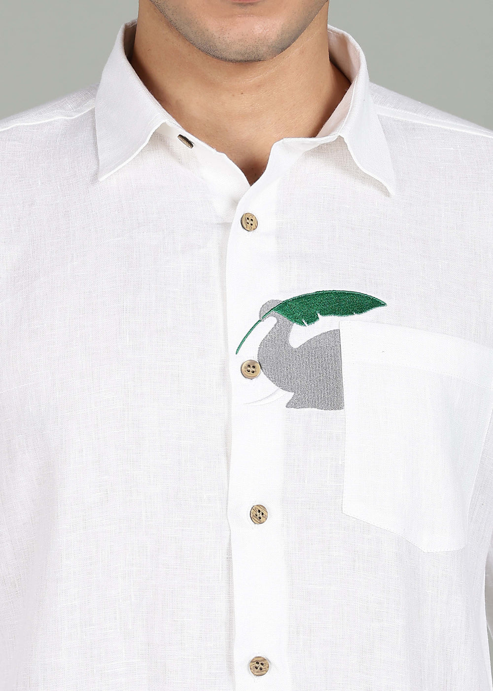 Man wearing a 100% pure linen white shirt in 44 LEA with elephant embroidery sitting on a chair against a gray background