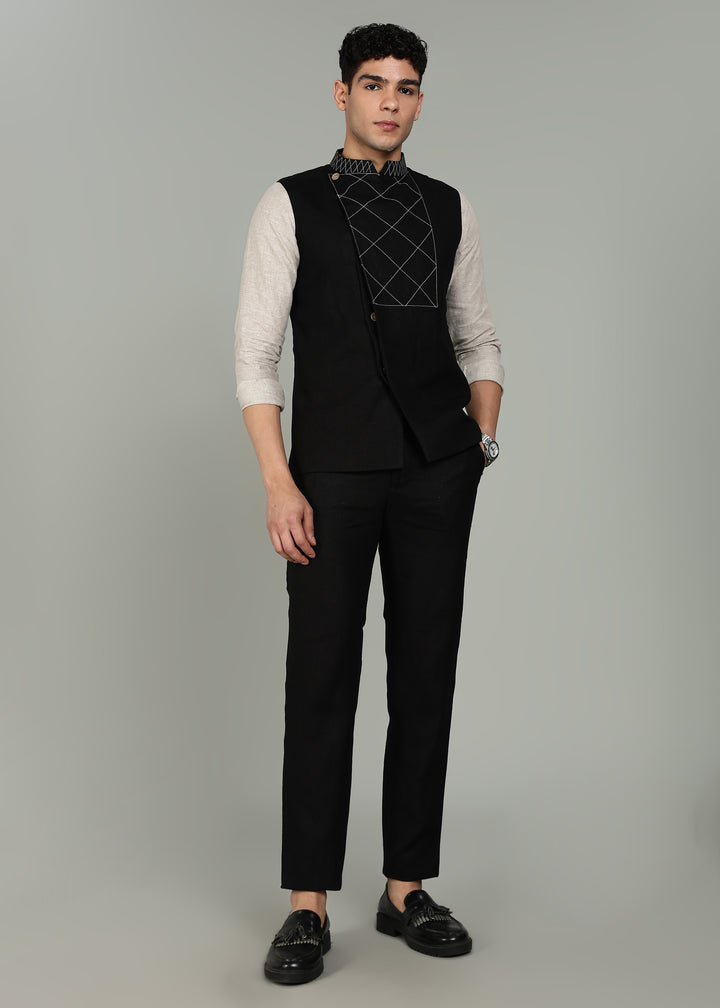 Man wearing a black embroidered 100% pure linen vest in 25 LEA over an ecru shirt on a gray background