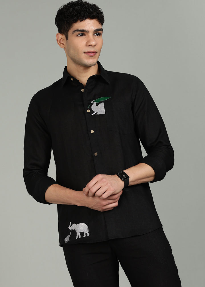 Man wearing a 100% pure linen black shirt in 60 LEA with elephant embroidery against a gray background