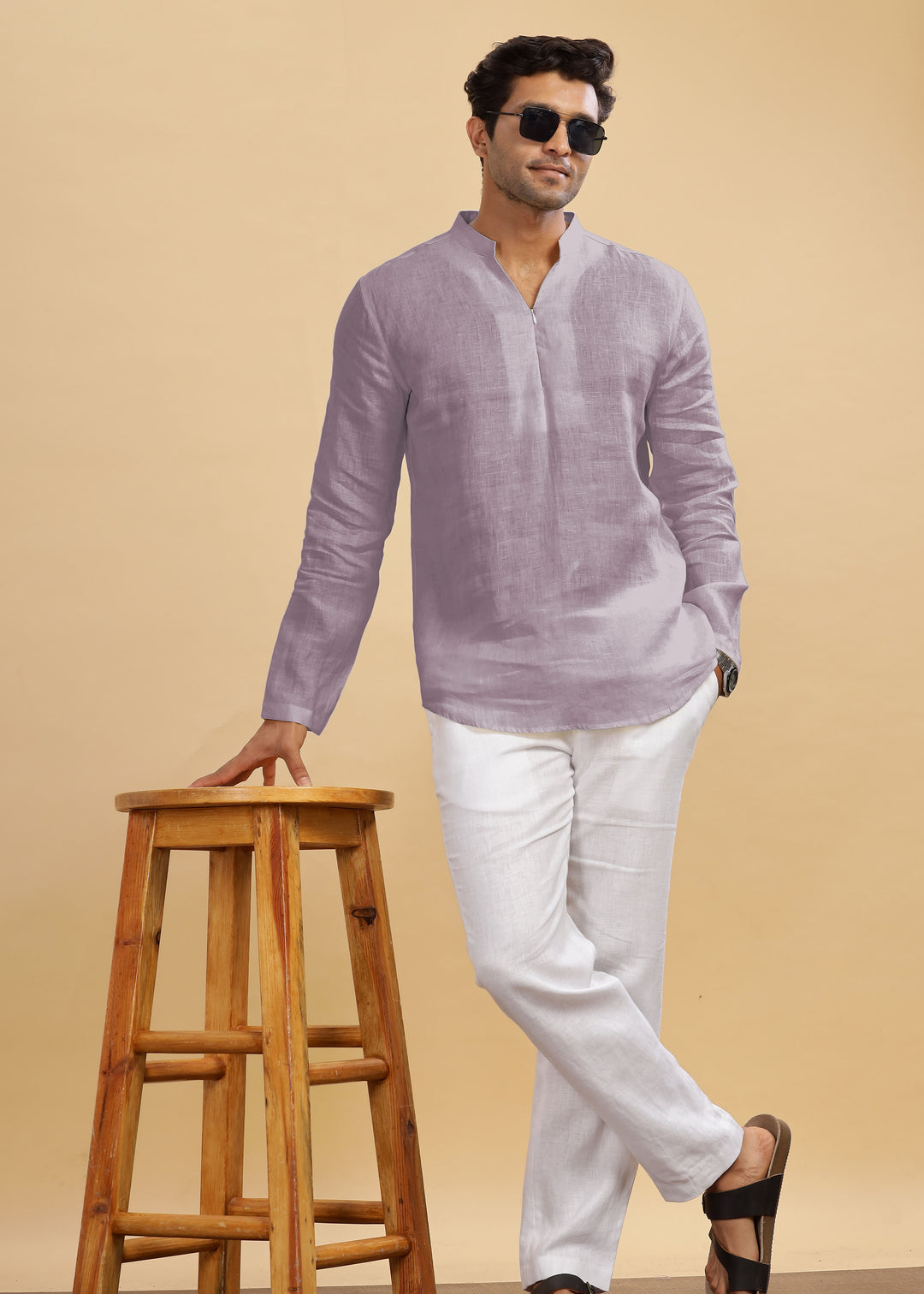 Man wearing a 100% pure linen cameo pink short kurta and white pants standing next to a wooden stool on a beige background
