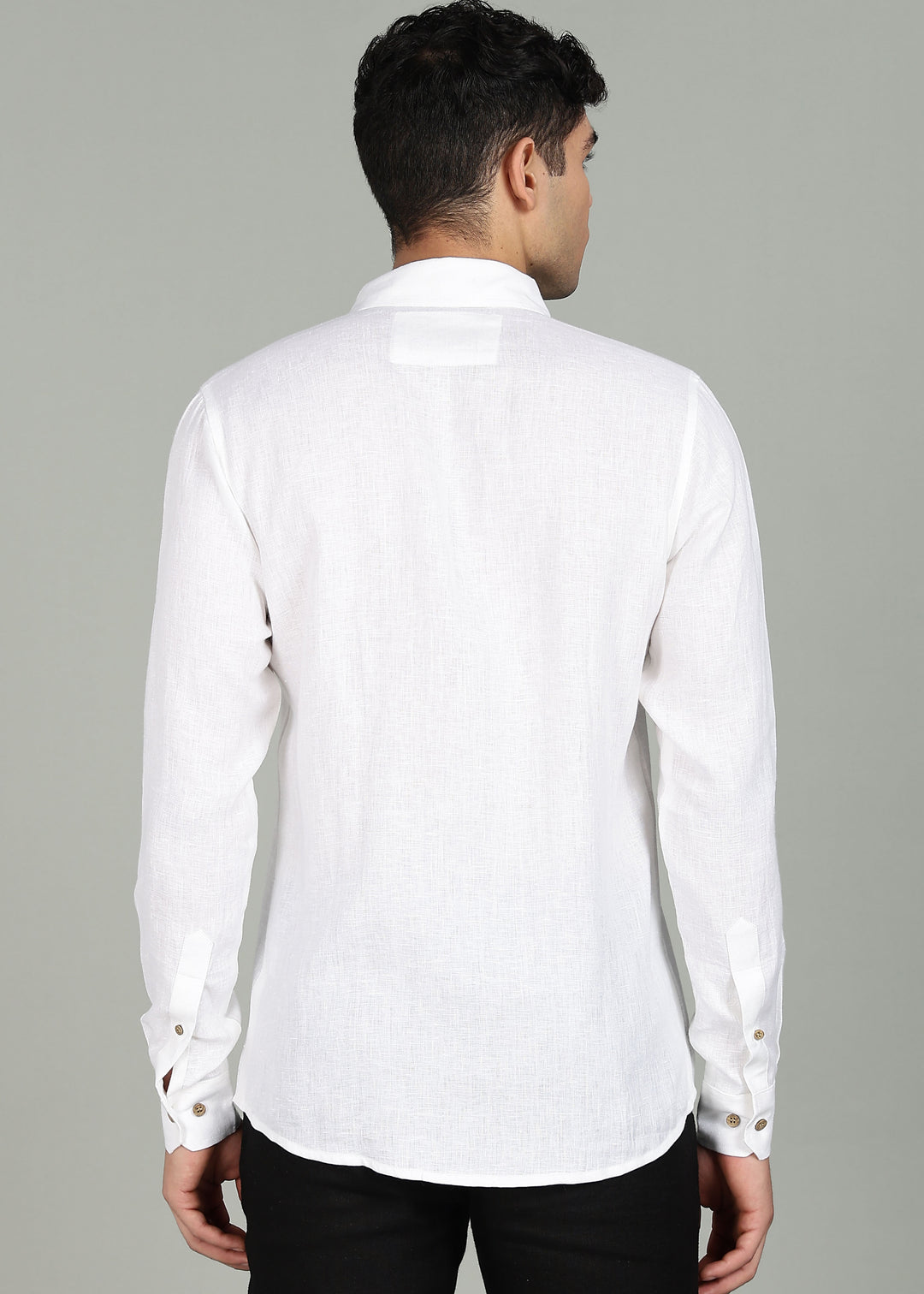 Man wearing a 100% pure linen white shirt in 44 LEA with elephant embroidery sitting on a chair against a gray background