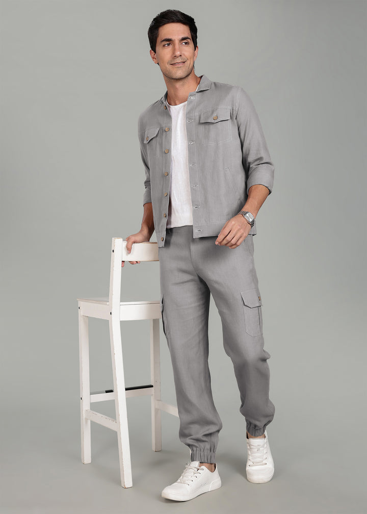 Man wearing a gray outfit with a white shirt, standing next to a white chair on a gray background