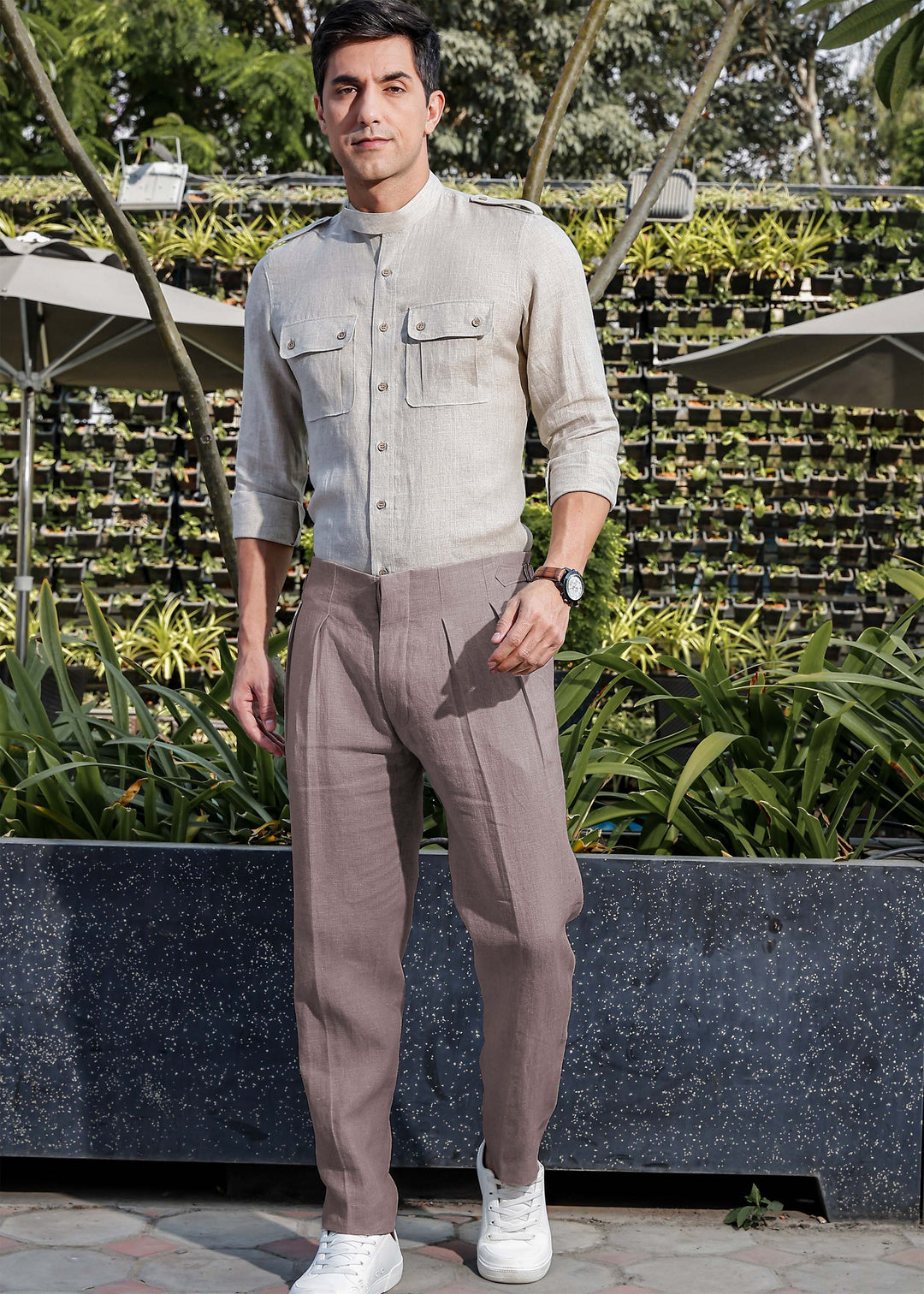 Man in 100% pure linen muted brown pants and ecru shirt standing outdoors with plants in the background