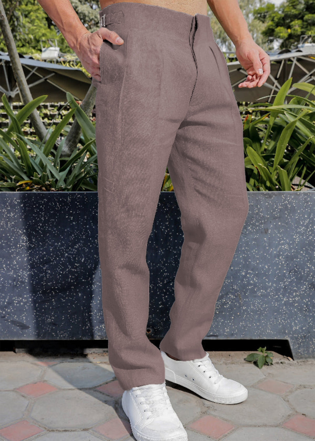 Person wearing 100% pure linen muted brown pants and white sneakers standing outdoors with plants in the background