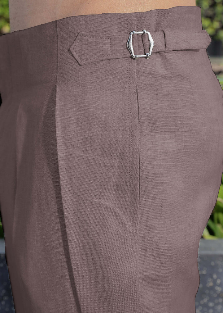 Close-up of 100% pure linen muted brown pants with a buckle against a blurred green background