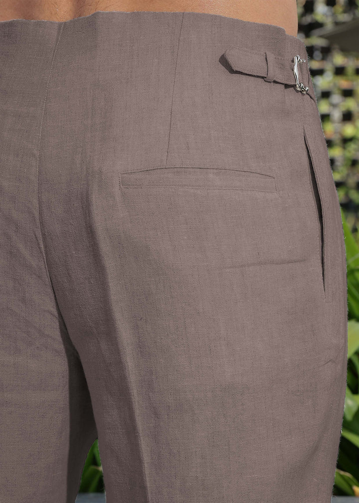 Close-up of 100% pure linen muted brown pants with a zipper pocket against a blurred green background