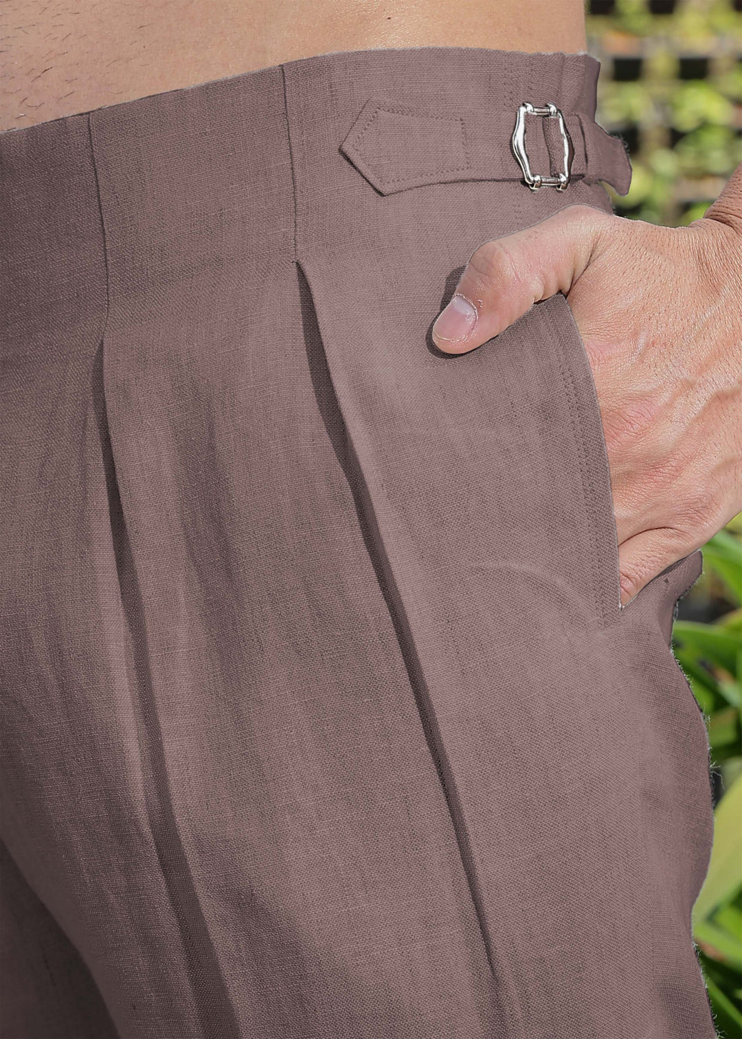 Close-up of 100% pure linen muted brown pants with a buckle detail, held by a hand.