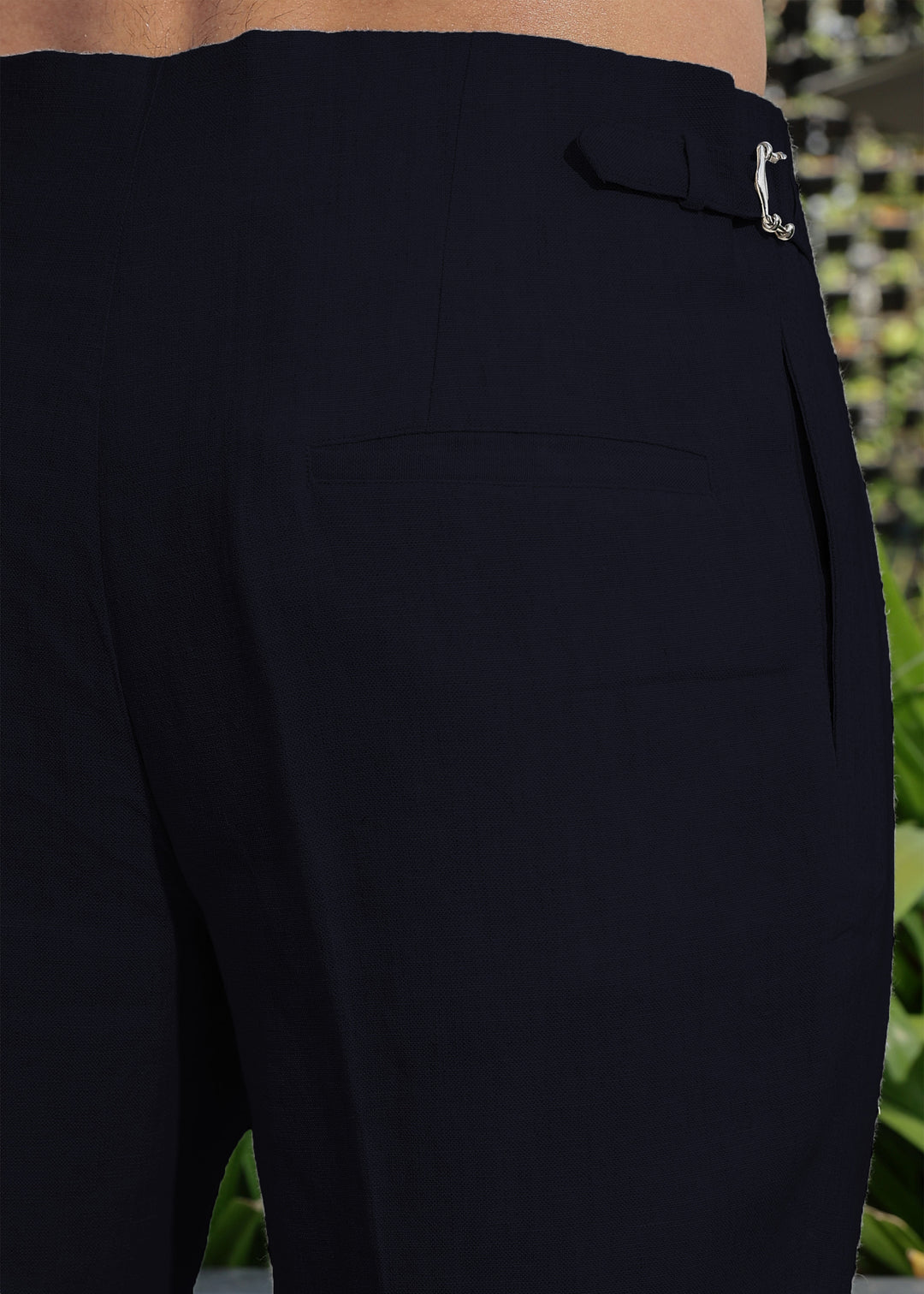 Close-up of 100% pure linen regal blue pants with a button detail, blurred green background