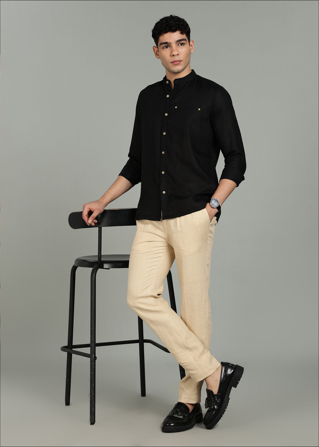 Man wearing a 100% pure linen black full sleeve shirt in 60 LEA, beige pants, and black shoes on a gray background