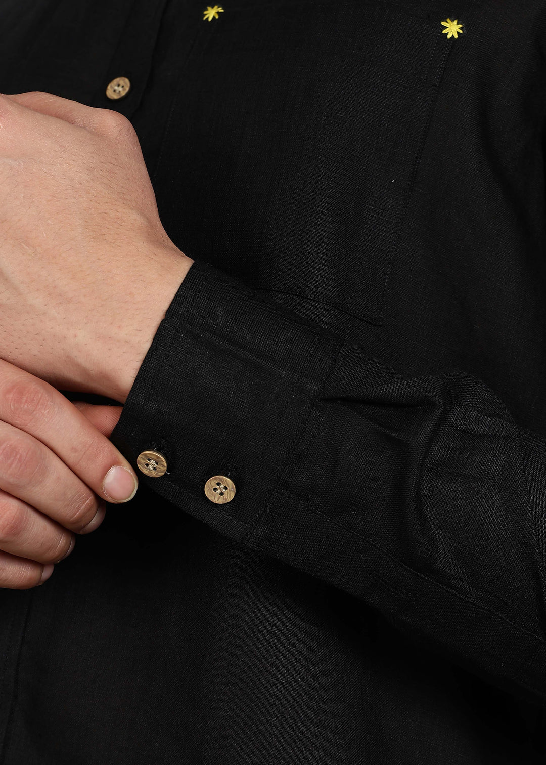 Close-up of a 100% pure linen black full sleeve shirt in 60 LEA with wooden buttons and yellow stars on a dark background