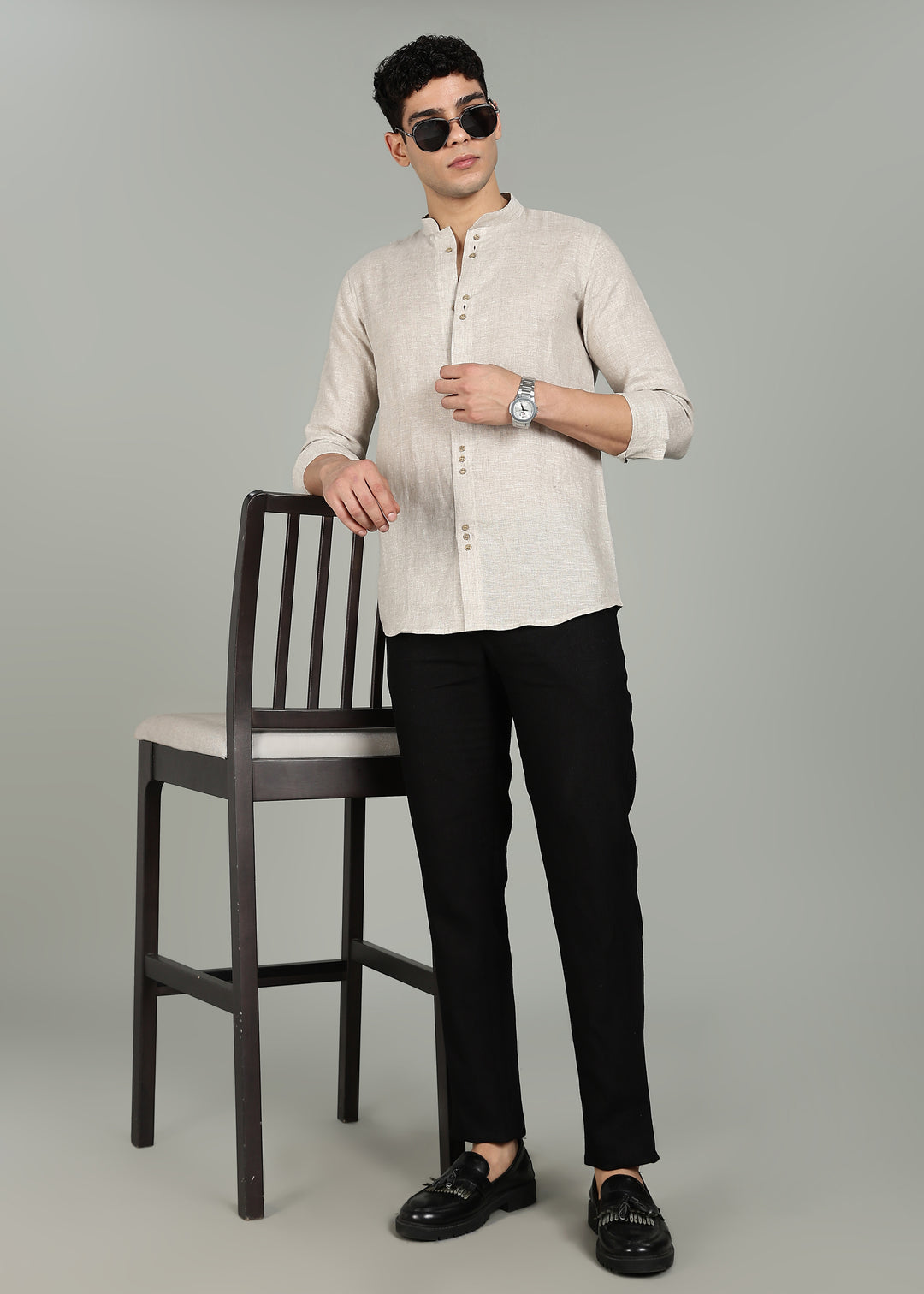 Man wearing a a 100% pure linen ecru full sleeve shirt in 60 LEA and black pants standing next to a chair on a gray background