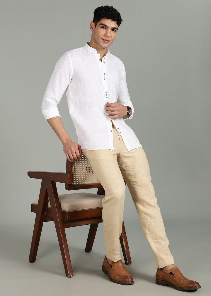 Man wearing a 100% pure linen white full sleeve shirt in 44 LEA and beige pants standing next to a wooden chair on a gray background