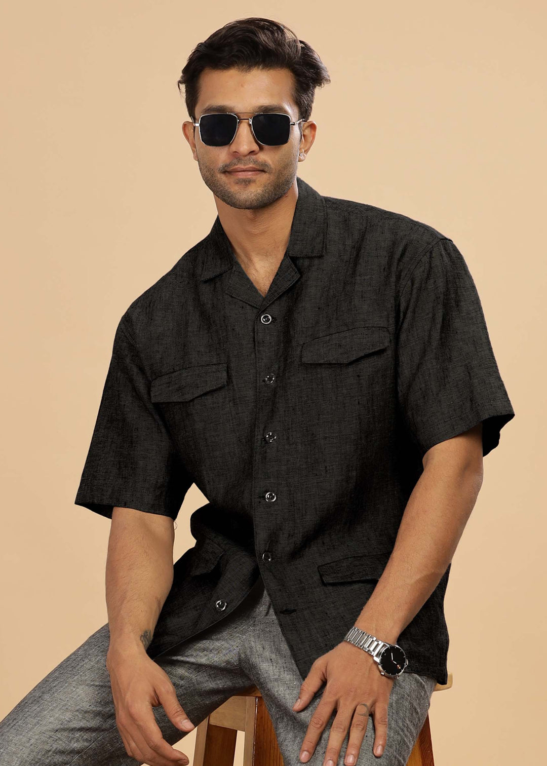 Man wearing a 100% pure linen black jacket in 25 LEA and sunglasses on a beige background