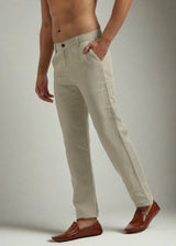 A pair of ecru-colored, pure linen trousers with a front fly closure and buttoned waistband, displayed on a male model wearing brown shoes.