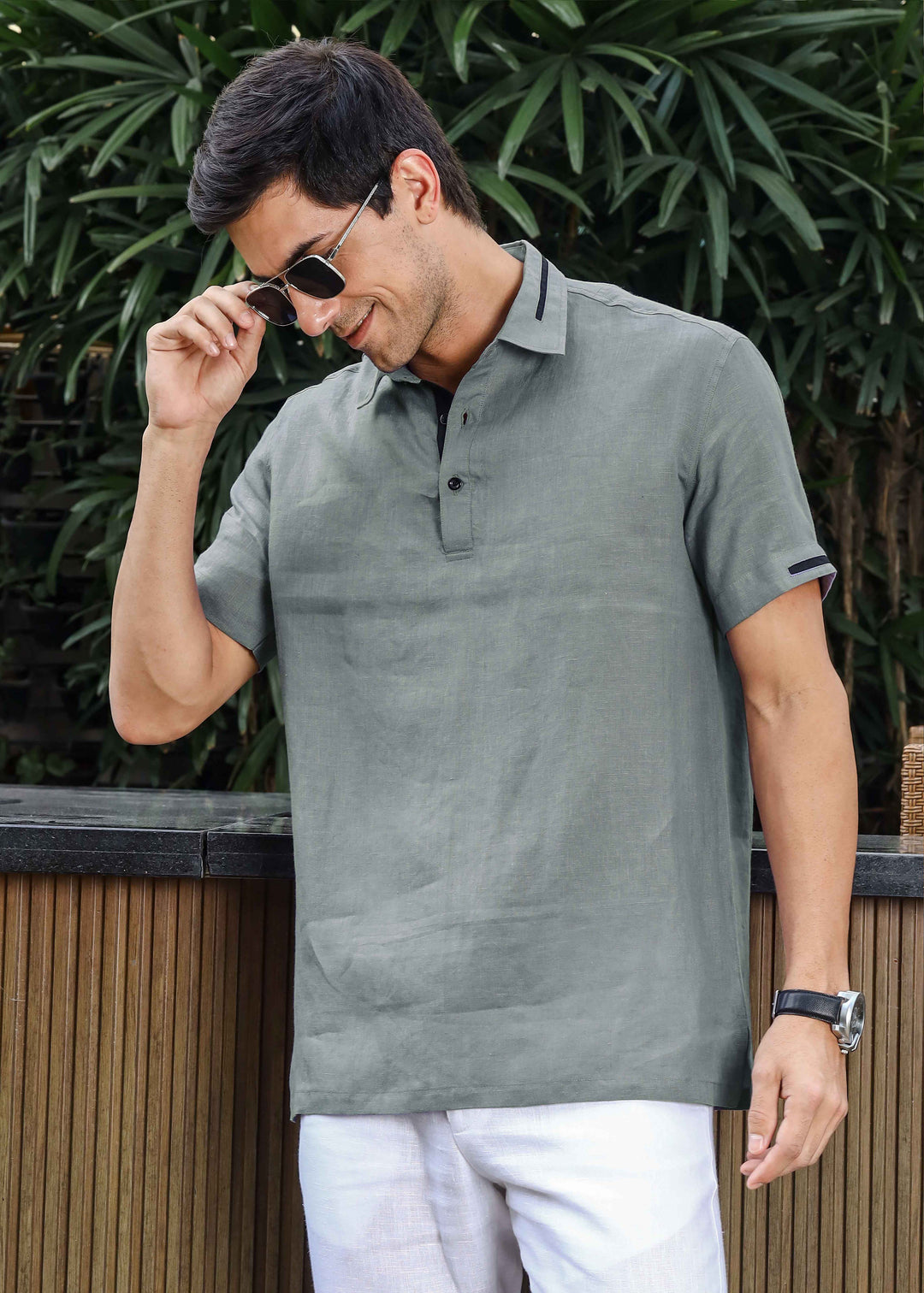 Man wearing a 100% pure linen gray t-shirt and white pants outdoors with greenery in the background